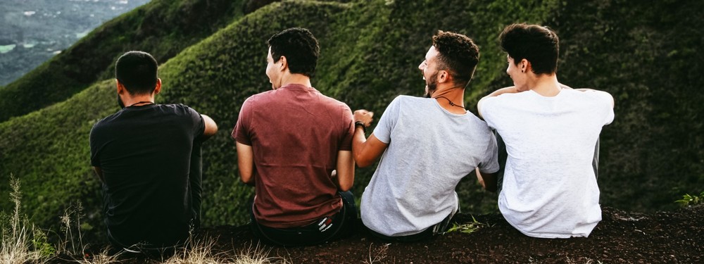 Four men sitting on a mountain, laughing and bonding